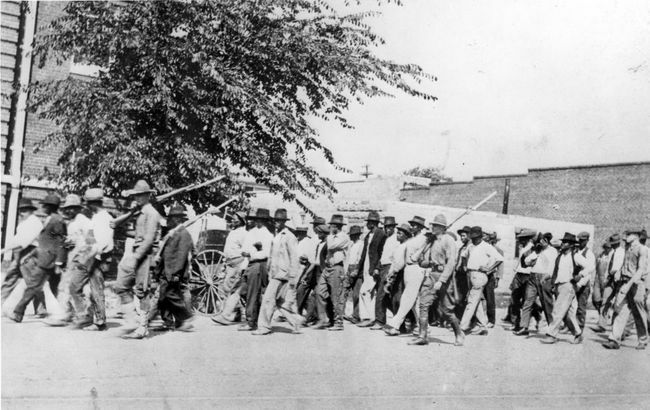 Група трупа Националне гарде, носећи пушке са причвршћеним бајонетима, прати ненаоружане црнце у притворски центар након масакра у Тулса Рацеу, Тулса, Оклахома, јун 1921.