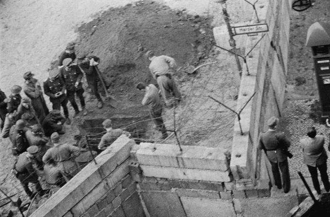 Група источноњемачких војника истражује тунел прокопан испод берлинског зида.